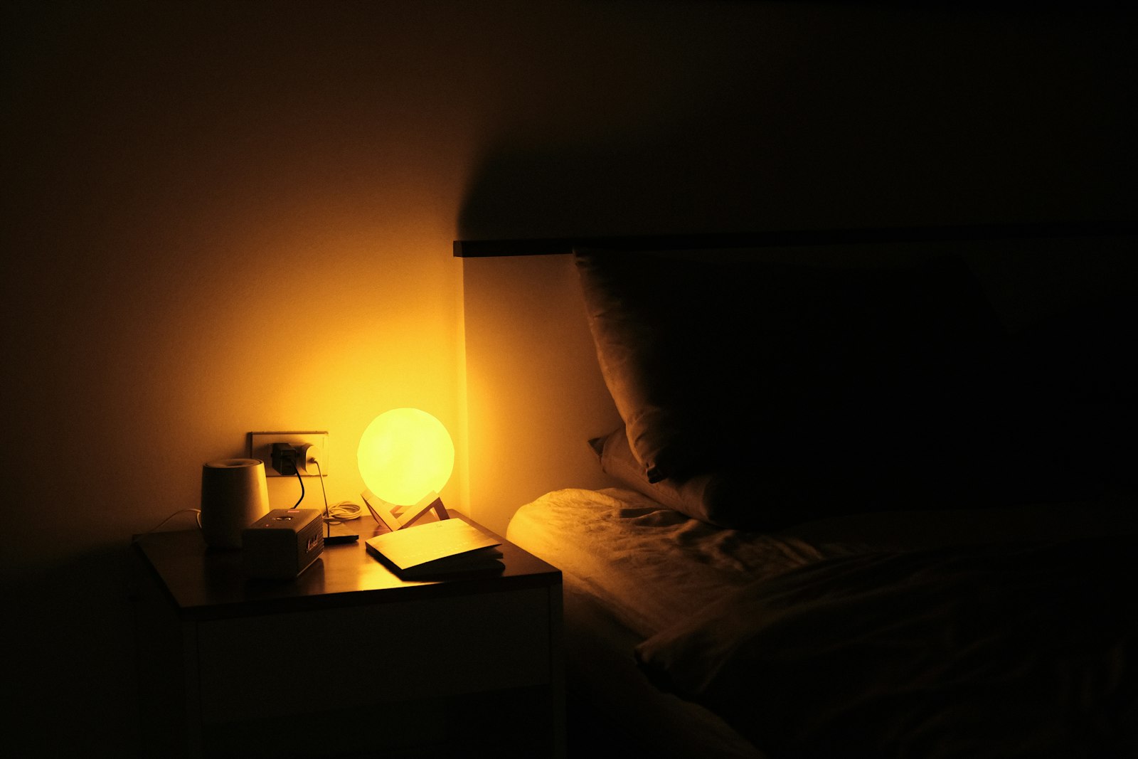 Dark bedroom with a glowing bedside lamp beside a bed.