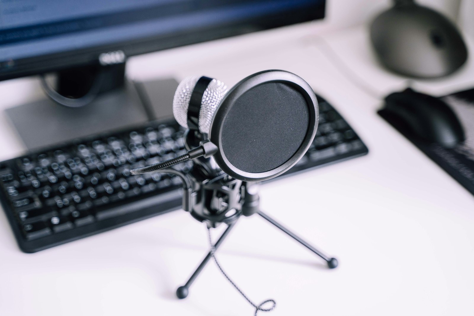 USB microphone on a desk in front of a keyboard and monitor.